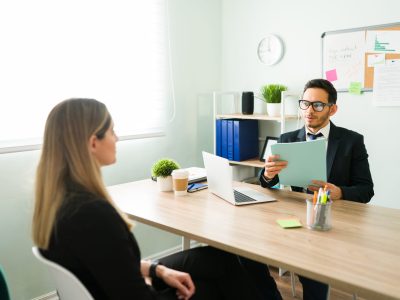 Caucasian young woman sitting with the human resources manager during a job interview. Male boss asking questions to a woman and holding her resume at the office